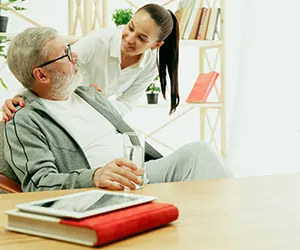 A woman is helping an older man with his glasses.