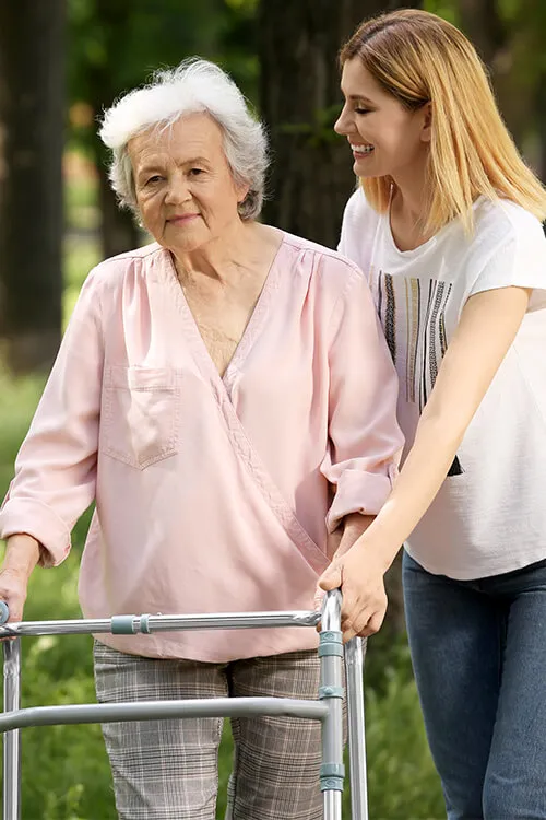 A woman helping an older person walk with a walker.