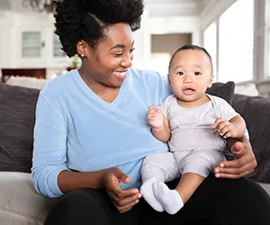 A woman holding a baby on the couch