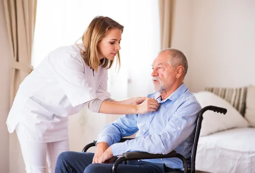 A nurse helping an elderly man in a wheelchair.