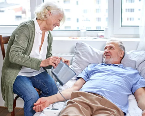 A woman is talking to an older man in bed.