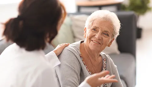 A woman talking to another person in front of a couch.