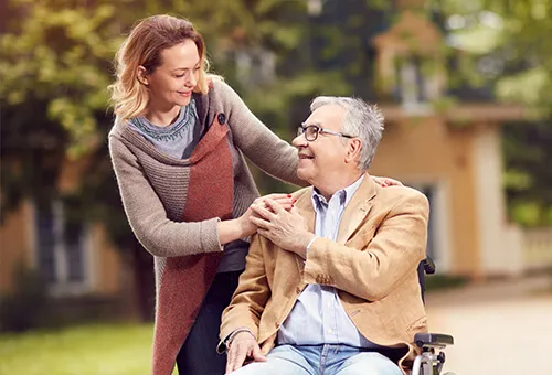 A woman is helping an older man in a wheelchair.