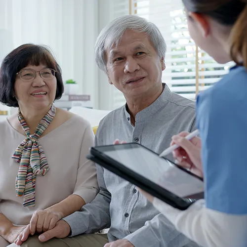 A woman is holding an ipad while two people sit at the table.