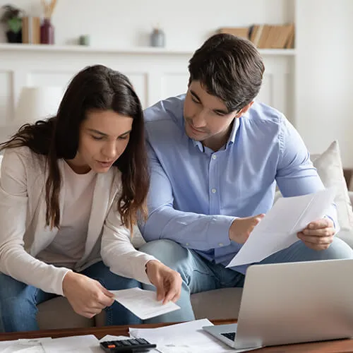 A man and woman sitting on the couch looking at papers.