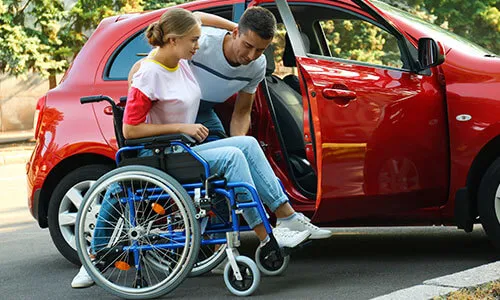 A man and woman in a wheelchair getting into a car.