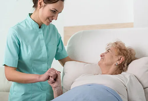 A nurse is holding the hand of an older woman.