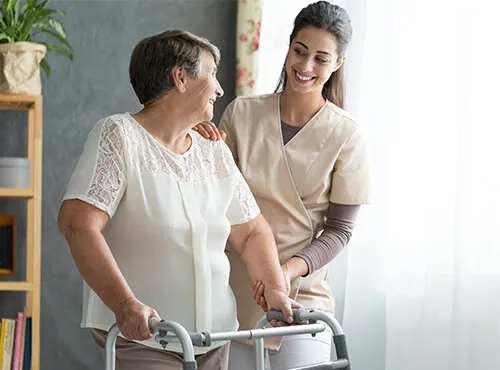 A woman helping an older person walk with a walker.