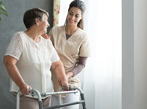 A woman in scrubs helping an older person walk.