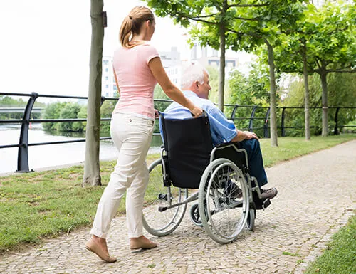 A woman pushing an elderly man in a wheelchair.