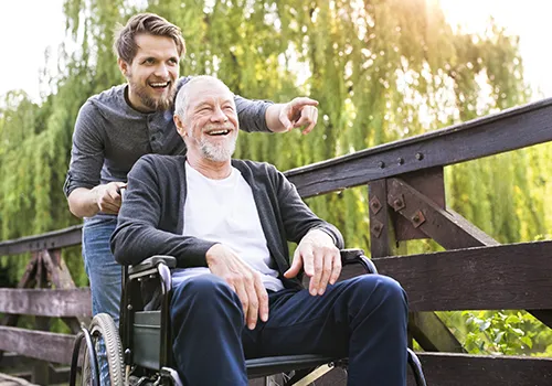 A man in a wheelchair and another man on a wooden bridge.