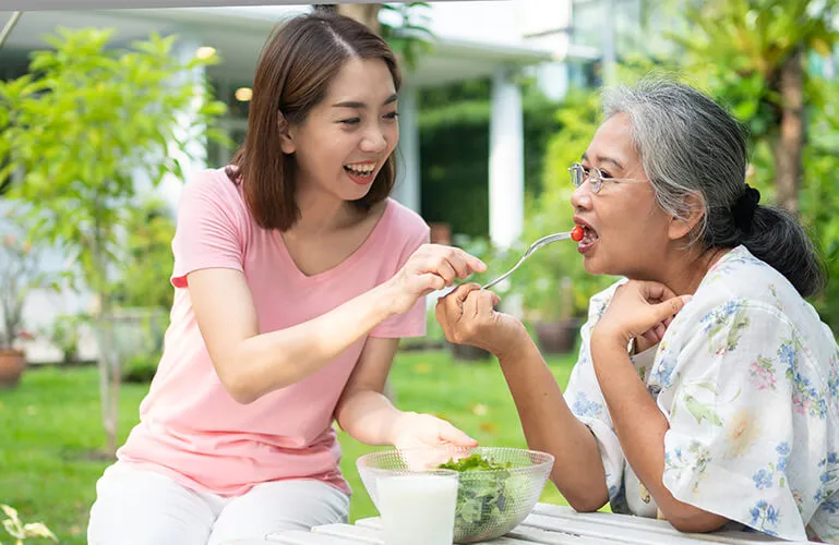 A woman and an older lady eating salad.