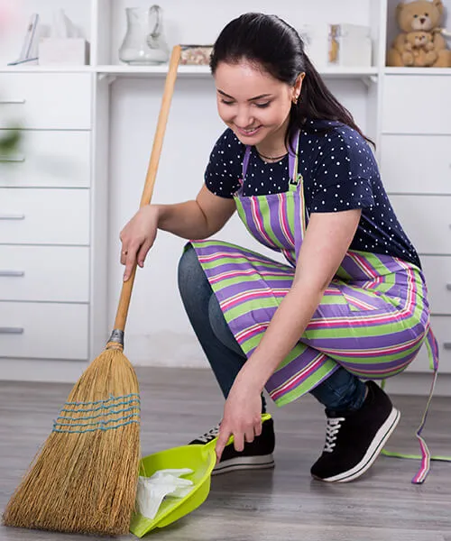 A woman is sweeping the floor with her broom.