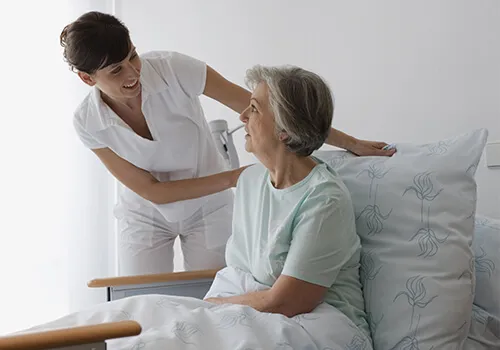 A nurse is helping an elderly woman in bed.