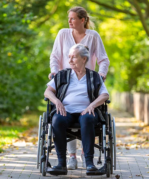 A woman pushing an elderly person in a wheelchair.