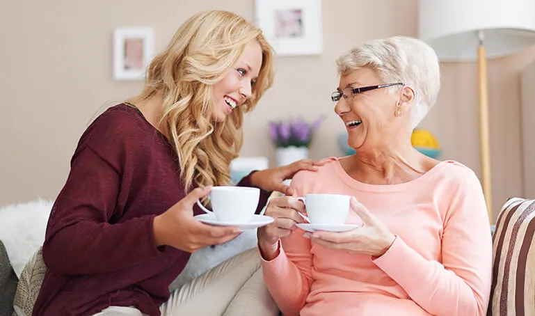 Two women sitting on a couch holding cups.