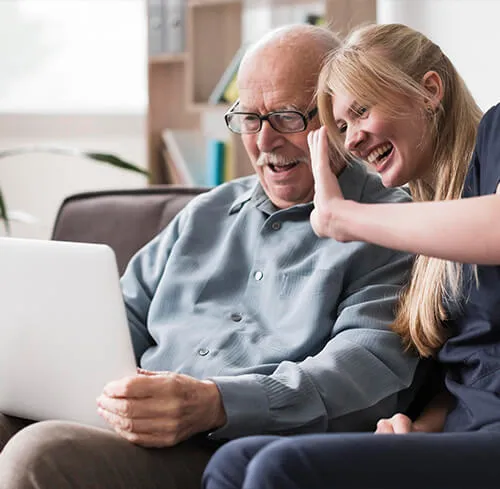 A woman and an old man sitting on the couch looking at a laptop.